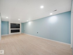 Spacious room featuring light wood-finish flooring, recessed lighting, and a built-in media center with white paneling - 