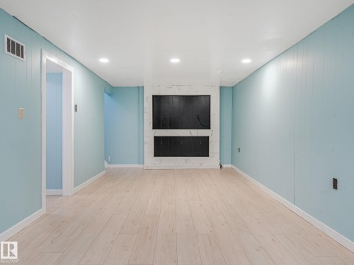Spacious room featuring wood-finish flooring, light blue vertical paneling, and a white ceiling with recessed lighting - 9315 151 Avenue, Edmonton, AB 