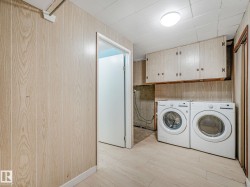 Dedicated laundry area featuring a pair of front-loading appliances, overhead cabinetry, wood-finish paneling, and light-toned flooring - 