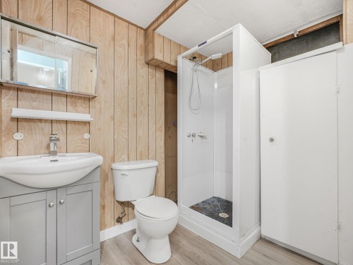 Bathroom featuring a white shower stall, wood-finish wall paneling, and a light gray vanity with a white countertop sink - 9315 151 Avenue, Edmonton, AB 