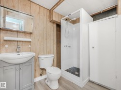 Bathroom featuring a white shower stall, wood-finish wall paneling, and a light gray vanity with a white countertop sink - 