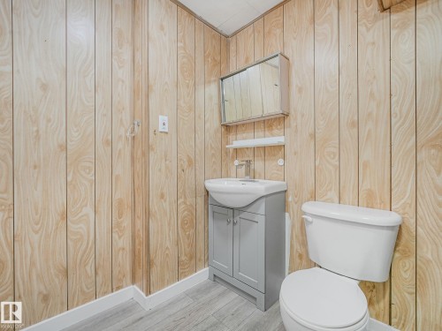 Bathroom featuring wood-look paneling, a gray vanity with an integrated sink, a mirrored medicine cabinet, a wall-mounted shelf, and light wood-finish flooring - 9315 151 Avenue, Edmonton, AB 