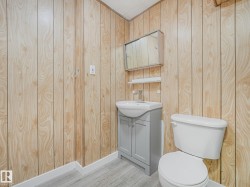 Bathroom featuring wood-look paneling, a gray vanity with an integrated sink, a mirrored medicine cabinet, a wall-mounted shelf, and light wood-finish flooring - 