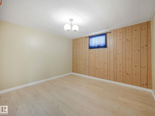 Spacious room featuring wood-finish flooring, two painted walls, and one wall with vertical wood paneling - 9315 151 Avenue, Edmonton, AB 