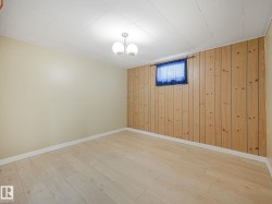 Spacious room featuring wood-finish flooring, two painted walls, and one wall with vertical wood paneling - 