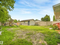 Expansive backyard with a mix of grass and soil, featuring a detached structure with a stucco and siding exterior, a wood fence, and mature trees providing natural screening - 