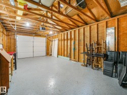 Spacious garage featuring exposed wood framing, an overhead garage door, and a light-colored epoxy floor coating - 