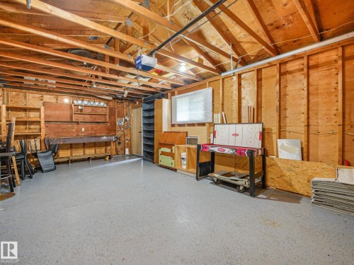 Garage space featuring exposed wood framing, a concrete floor, built-in shelving, a workbench, and a window with blinds - 9315 151 Avenue, Edmonton, AB 