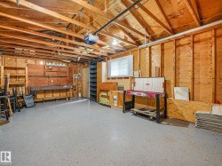 Garage space featuring exposed wood framing, a concrete floor, built-in shelving, a workbench, and a window with blinds - 