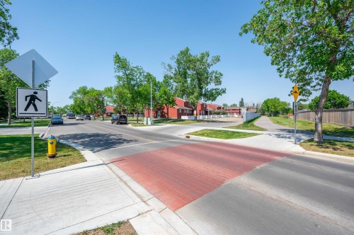 Red brick crosswalk, paved road, concrete sidewalks, pedestrian crossing signage, and mature trees - 10678 Beaumaris Road Nw, Edmonton, AB 