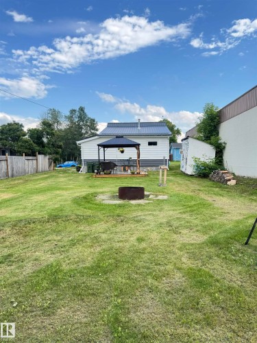 Expansive backyard with a manicured lawn, a fire pit area, and a white shed - 4912 49 Avenue, Onoway, AB 