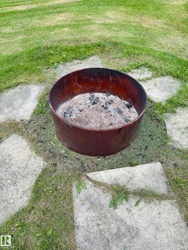 Circular metal fire pit on a stone paver base, surrounded by a grass lawn - 4912 49 Avenue, Onoway, AB 