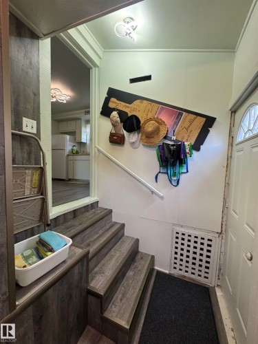 Stairwell featuring wood-finish flooring, a white handrail, and a white entrance door with an arched window insert - 4912 49 Avenue, Onoway, AB 