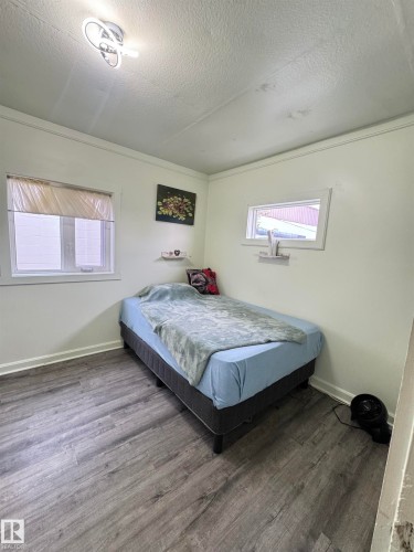 Room featuring gray wood-finish flooring, two window units, and a contemporary flush-mount ceiling light fixture - 4912 49 Avenue, Onoway, AB 
