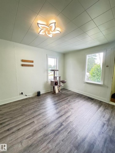 Spacious interior featuring wood-finish flooring, white walls, and two large windows - 4912 49 Avenue, Onoway, AB 