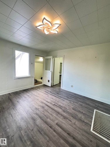 Spacious room featuring wood-finish flooring, white trim, and a decorative ceiling light fixture - 4912 49 Avenue, Onoway, AB 