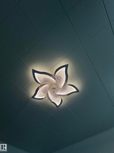 Decorative ceiling light fixture with petal-shaped diffusers, central bulb, and backlighting, set against a textured ceiling - 4912 49 Avenue, Onoway, AB 