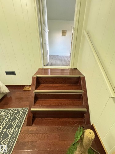 Rich wood-finish stairs featuring metallic stair rods which accents the sunken second bedroom - 4912 49 Avenue, Onoway, AB 