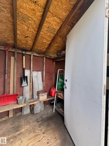 Storage shed interior featuring exposed wood framing, an angled roofline with oriented strand board sheathing, a built-in wooden shelf, and a painted door - 4912 49 Avenue, Onoway, AB 