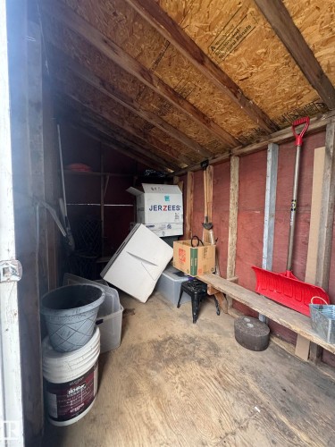 Utility shed interior featuring exposed wood framing, plywood flooring, and a built-in wooden shelf - 4912 49 Avenue, Onoway, AB 