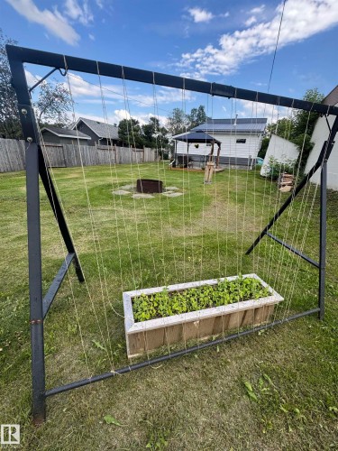 Landscaped backyard featuring a built-in fire pit with paver surround, a covered gazebo, and a vertical garden structure with vines planted. - 4912 49 Avenue, Onoway, AB 