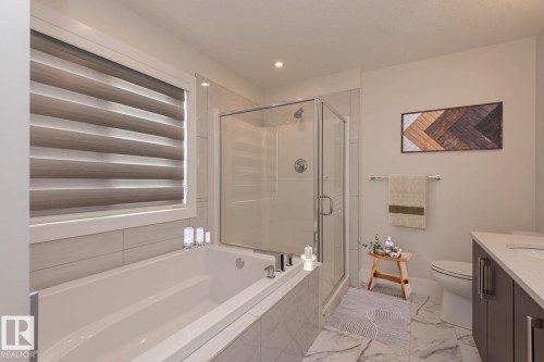 Bathroom featuring a built-in soaking tub, glass-enclosed shower, and a single vanity with a solid surface countertop - 2635 Donaghey Crescent, Edmonton, AB 