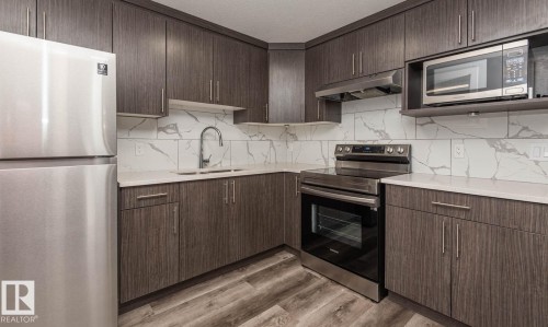 Contemporary kitchen featuring wood-finish cabinetry, stainless steel appliances, a white veined backsplash, light-toned countertops, and wood-look flooring - 2635 Donaghey Crescent, Edmonton, AB 