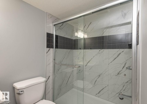 Shower enclosure featuring sliding glass doors, white marble-look tile, and a dark accent tile band - 2635 Donaghey Crescent, Edmonton, AB 