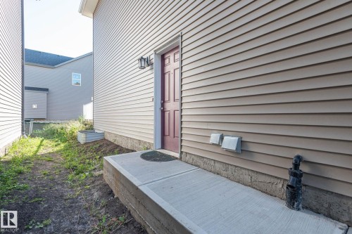 Exterior side entrance with a concrete walkway, light-toned horizontal siding, and a red paneled door - 2635 Donaghey Crescent, Edmonton, AB 