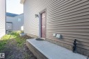 Exterior side entrance with a concrete walkway, light-toned horizontal siding, and a red paneled door - 2635 Donaghey Crescent, Edmonton, AB 