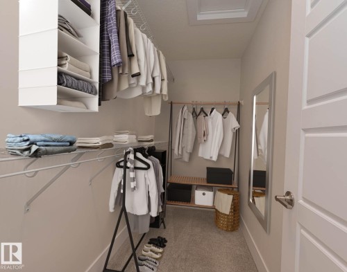 Walk-in closet featuring built-in wire shelving, hanging rods, carpet flooring, a flush-mount ceiling light fixture, and a white paneled door with a brushed nickel handle - 2635 Donaghey Crescent, Edmonton, AB 