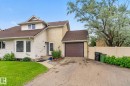 Exterior featuring light-colored siding and stucco finishes, a prominent bay window, an integrated single-car garage with a brown door, a front entry with a small porch, and a dormer window - 9503 180A Street Nw, Edmonton, AB  - Outdoor 