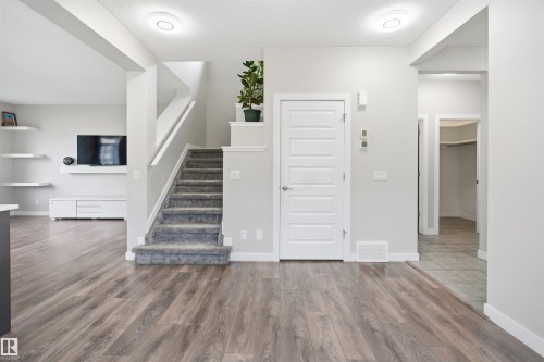 Open-concept main level featuring wood-finish flooring, a carpeted staircase with white railings, and a panel door with brushed nickel hardware - 1234 Daniels Crescent, Edmonton, AB - Indoor Photo Showing Other Room