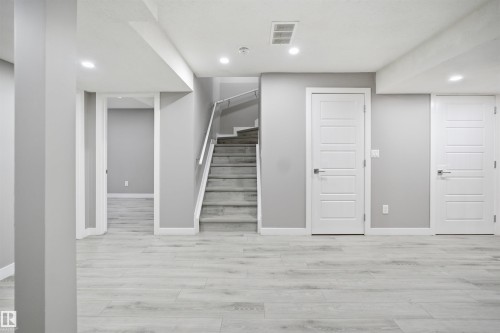 Versatile lower level featuring light wood-finish flooring, recessed lighting, and a staircase with a glass and metal railing - 1234 Daniels Crescent, Edmonton, AB - Indoor Photo Showing Other Room