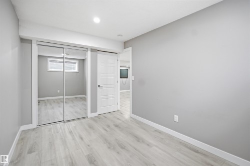 Light gray walls complement wood-finish flooring in this room featuring a mirrored closet with sliding doors and a white paneled door - 1234 Daniels Crescent, Edmonton, AB - Indoor Photo Showing Other Room