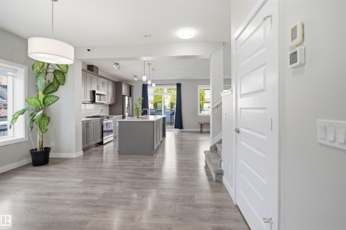 Spacious living area featuring wood-finish flooring, a contemporary kitchen with gray cabinetry and stainless steel appliances, a central island, and abundant natural light from large windows - 1234 Daniels Crescent, Edmonton, AB - Indoor Photo Showing Kitchen