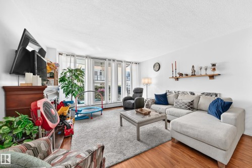Living area with wood-finish flooring, a built-in fireplace, and expansive windows - #407 9835 113 St Nw, Edmonton, AB 