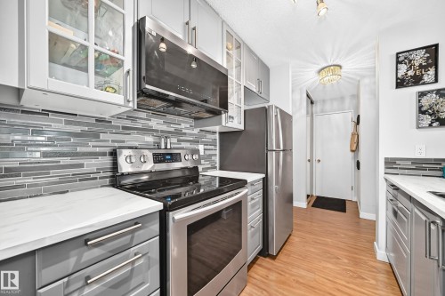Open-concept kitchen and dining area featuring laminate flooring, recessed lighting, track lighting, and a kitchen with gray cabinetry, stainless steel appliances, and a tiled backsplash - #407 9835 113 St Nw, Edmonton, AB 