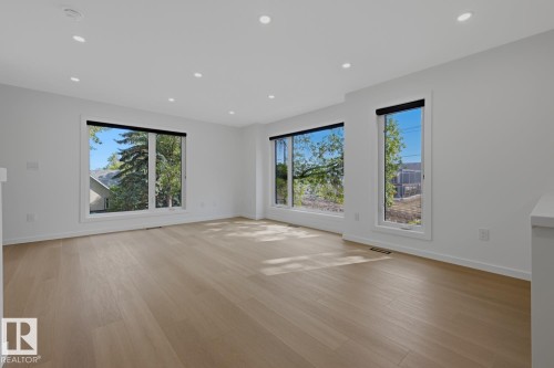 Bright interior space featuring light wood-finish flooring, white walls, and multiple large windows with black roller shades - 8903 94 Ave Nw, Edmonton, AB 