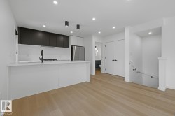 Modern kitchen featuring a white island with a matte black faucet, dark flat-panel cabinetry, stainless steel appliances, and recessed lighting - 