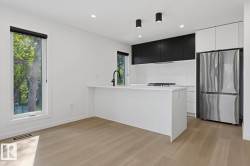 Modern kitchen featuring a white island with an integrated sink and matte black faucet, stainless steel French door refrigerator, and contrasting black and white cabinetry - 