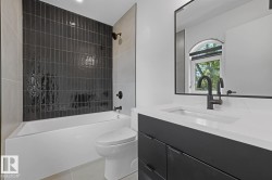 Bathroom featuring a built-in tub with dark vertical subway tile surround and matte black fixtures - 