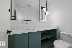 Modern bathroom featuring a white countertop with an integrated rectangular sink, wall-mounted faucets, a black-framed mirror, and a contemporary pendant light fixture - 