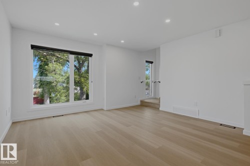 Spacious room featuring light wood-finish flooring, recessed ceiling lighting, and large windows with black roller shades - 8903 94 Ave Nw, Edmonton, AB 