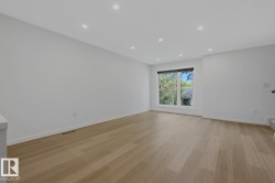 Spacious room featuring light wood-finish flooring, recessed lighting, a large window, and crisp white walls - 
