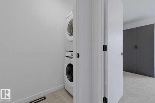 Dedicated laundry area featuring a stacked washer and dryer, light-toned flooring, and neutral wall finishes - 8903 94 Ave Nw, Edmonton, AB 