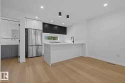 Contemporary kitchen featuring a white island with a matte black faucet, stainless steel refrigerator, and integrated cooktop - 