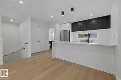 Modern kitchen featuring a waterfall island with a matte black faucet, integrated cooktop, and white countertop - 