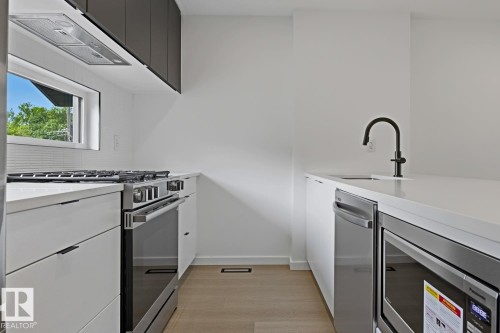 Contemporary kitchen featuring white cabinetry, light countertops, and wood-finish flooring - 8903 94 Ave Nw, Edmonton, AB 