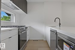 Contemporary kitchen featuring white cabinetry, light countertops, and wood-finish flooring - 